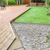 A dog on a wooden deck next to a gravel border and artificial grass. Voir les images du produit