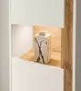 A close-up view of a modern white cabinet with a wood-effect interior shelf, featuring a decorative vase with black abstract markings. Produktbild-Vorschau