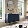 A dark blue dresser with gold legs and handles is placed in a well-lit room with large windows. Podgląd zdjęcia produktu