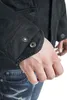 Close-up of a person's arm wearing a black jacket with buttons on the cuff, and blue jeans. Produktbild-Vorschau