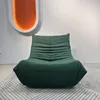 A green sofa chair is placed on a rug in front of a white wall with an abstract orange light fixture. Voir les images du produit