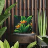 A pillow with a Strelitzia flower pattern is placed on a wooden side table, surrounded by lush green plants. Produktbild-Vorschau