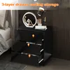 A black bedside table with three open drawers, displaying decorative items and books on top. Produktbild-Vorschau