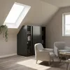 A modern attic bedroom with a slanted ceiling, featuring a dark gray sliding door wardrobe designed for sloped walls, two beige armchairs, and a round wooden coffee table. Anteprima dell’immagine prodotto