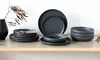 A set of dark gray stoneware plates and bowls are arranged on a wooden shelf, with a dried plant branch in a black vase to the left. Podgląd zdjęcia produktu