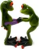 Two green frog figurines with orange eyes and red toes are positioned facing each other. One frog is wearing purple shorts, and the other frog is holding the shorts. Produktbild-Vorschau