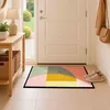 A doormat with a geometric pattern is placed in front of a white door in a hallway. A wooden console table with baskets and a lamp is on the left, and a coat and handbag are hanging on the wall to the right. A pair of sneakers is placed next to the doormat Produktbild-Vorschau