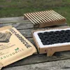 A disposable barbecue and its packaging are laid out on a wooden picnic table outdoors. Produktbild-Vorschau