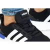 Close-up of a person wearing black Adidas sneakers with white stripes and blue accents. Podgląd zdjęcia produktu