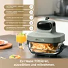 A close-up of a green air fryer on a kitchen counter, with a glass of orange juice and some food in the background. Produktbild-Vorschau