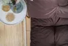 A top-down view of brown cushions on a pallet, next to a small white table with coasters and a vase. Anteprima dell’immagine prodotto