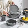 A person is arranging a set of grey ceramic dishes on a table. Produktbild-Vorschau