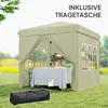 A beige pop-up gazebo set up on a grassy lawn with a table and chairs inside, and a black carrying bag in the foreground. Náhled obrázku produktu