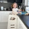 A young girl is in a kitchen, standing on a learning tower and preparing food. Náhled obrázku produktu