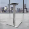 A table base with a square foot and a cylindrical column, placed on a concrete floor in front of a large window overlooking a city skyline at dusk. Anteprima dell’immagine prodotto
