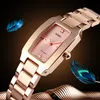 A close-up, angled shot of a rose gold SKMEI women's watch with a pink dial, set against a dark, gradient background with decorative feathers and wavy metallic elements. Produktbild-Vorschau
