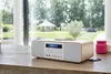 A Thomson micro-stereo system is placed on a wooden table in front of a large window overlooking a garden. Produktbild-Vorschau