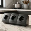 A black power strip with three outlets sits on a marble countertop in a kitchen setting. Náhled obrázku produktu