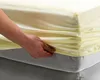 A hand is shown tucking a yellow fitted sheet onto a gray mattress. Produktbild-Vorschau