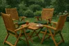 A wooden table and chairs set with green cushions arranged on a lawn, with a drink and a cup of coffee on the table. Produktbild-Vorschau