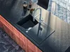 A modern kitchen island with a black granite countertop, a black sink, and a sleek faucet. There is a French press and a cup of coffee on the counter. Produktbild-Vorschau