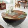 A round coffee table with a reclaimed wood top and a dark bowl-shaped base, placed in a living room setting with a desk and chair in the background. Produktbild-Vorschau