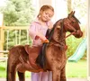 A young girl is brushing the mane of a plush rocking horse outdoors. Produktbild-Vorschau