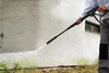 A person is using a pressure washer to clean the exterior wall of a building. Produktbild-Vorschau