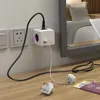 A white power cube adapter plugged into a wall socket, with a black power cord and a white USB cable plugged into it. Two white travel plugs are on the wooden surface in the foreground, along with a passport and a yellow document. Produktbild-Vorschau