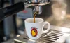 Espresso being brewed into a white mug with a logo. Produktbild-Vorschau