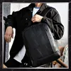 A man wearing a black jacket and white t-shirt is holding a black rucksack over his shoulder. Anteprima dell’immagine prodotto