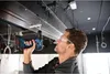 A man is using a cordless drill to attach something to a ceiling structure. Voir les images du produit