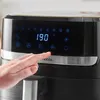 A close-up of a person's finger pressing a button on the digital display of a black air fryer. Produktbild-Vorschau