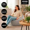 A woman is sitting on a large gray beanbag chair in a living room setting. Voir les images du produit