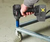 A person is using a cordless impact wrench to tighten a bolt on a metal frame with wheels. Produktbild-Vorschau