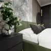 A close-up view of a bedroom with a green upholstered bed, white bedding, and a bedside table with a vase of flowers. Náhled obrázku produktu