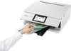 A hand is shown inserting a document into a white Canon PIXMA TS8751 WLAN color multifunction photo printer. Podgląd zdjęcia produktu