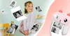 A young girl is smiling and looking away from the camera, with several printed photos floating around her. A pink instant camera is shown on the right side of the image. Anteprima dell’immagine prodotto