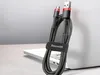 A black and red braided micro USB data cable is coiled and held together by a velcro strap with the brand name 'Baseus' printed on it. The cable is placed on a laptop. Náhled obrázku produktu