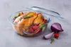 A roasted chicken with vegetables in a glass casserole dish, with red onion and a tomato on the side. Produktbild-Vorschau