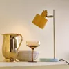 A table lamp with a yellow shade sits on a shelf next to a gold pitcher, a glass, and a bowl. Produktbild-Vorschau