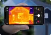 A hand holding a smartphone with a thermal imaging app displaying a house. Voir les images du produit