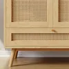 A close-up view of the lower section of a wooden cabinet with rattan detailing. Náhled obrázku produktu