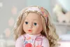 Close-up of a Baby Annabell Sophia doll with blonde hair and blue eyes, wearing a pink shirt with floral and butterfly designs. Produktbild-Vorschau