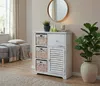 A hallway or living room setting with a white distressed cabinet with wicker baskets and a louvered door, a round mirror, a plant, and a bench with a blanket. Produktbild-Vorschau