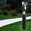 A modern outdoor lamp post with three illuminated columns stands on a green lawn next to a paved walkway. Produktbild-Vorschau
