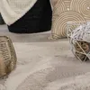 A close-up view of a textured beige rug with decorative objects on it, including a gold candle holder and a white wire basket with decorative balls. Produktbild-Vorschau