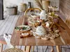 A wooden table set with various tableware items, including a butter dish, plates, glasses, and crackers, arranged for a meal. Produktbild-Vorschau
