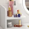 A close-up view of a white shelf displaying various cosmetic products, including bottles, lipstick, and an eyeshadow palette. Podgląd zdjęcia produktu