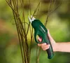 A hand holding a green electric garden shear to cut branches of a plant. Produktbild-Vorschau
